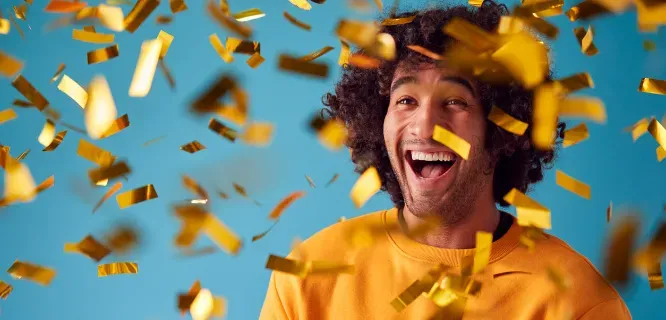 Hombre celebrando entre confeti dorado con expresión de alegría y felicidad